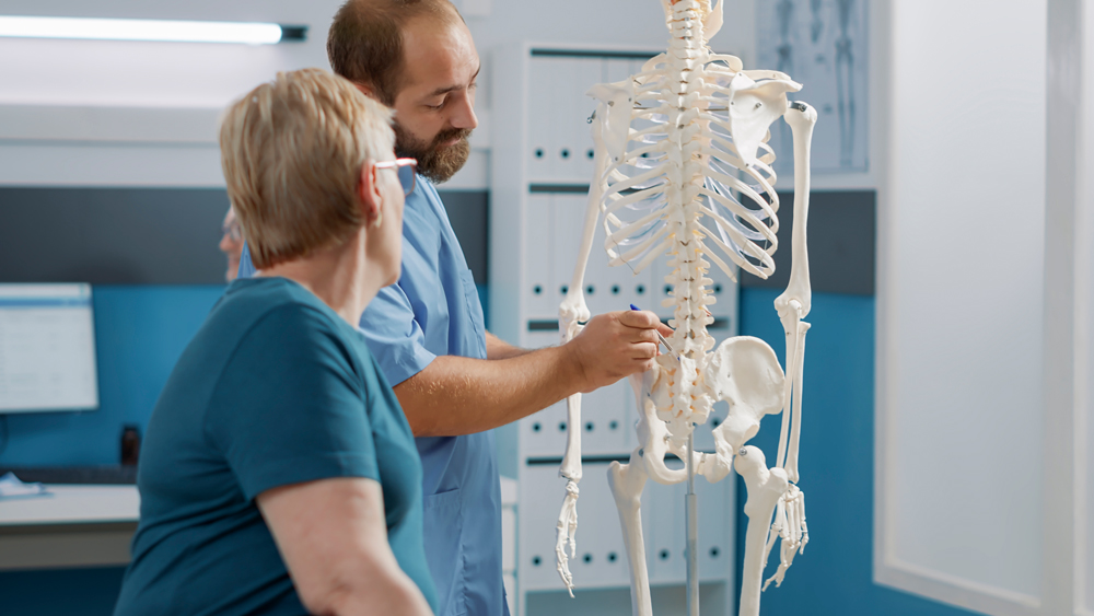 male-doctor-pointing-human-skeleton-show-spinal-cord-explain-mechanical-disorders-rehabilitation-cabinet-specialist-explaining-back-bones-system-physical-therapy
